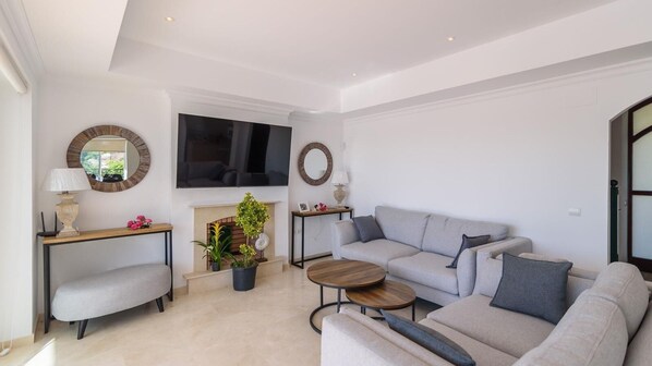 A modern living room with a grey sofa, a coffee table, a fireplace, and a TV mounted on the wall. - Villa Latina Golf Arcos de la Frontera by Ruralidays (Cádiz)
