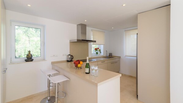 A modern kitchen with a central island, bar stools, a kettle, a fruit bowl, and a bottle of wine. - Villa Latina Golf Arcos de la Frontera by Ruralidays (Cádiz)
