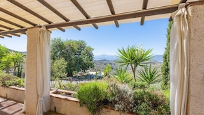A covered outdoor area with a view of a mountainous landscape, surrounded by various plants and a pergola structure. - Finca Las Nuevas, Casa Carmen Álora by Ruralidays (Málaga)