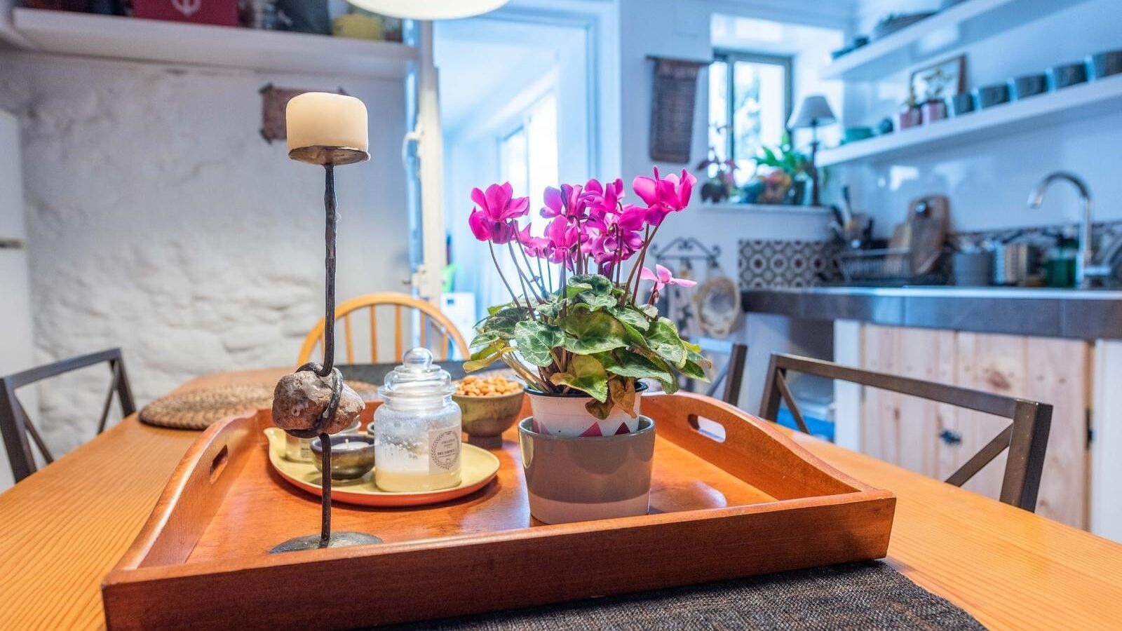 A wooden dining table with a tray, a candle, a potted plant, and a jar of honey.