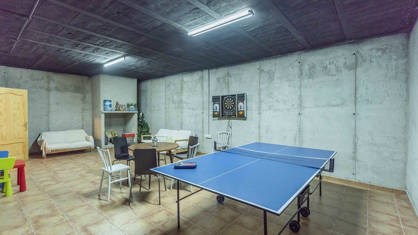 Een kamer met een tafeltennistafel, stoelen, een klein tafeltje met een lamp en een bed.