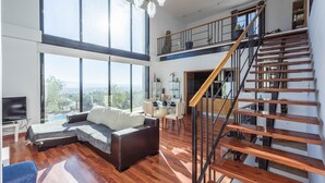 A spacious living room with a large window, a sofa, a TV, and a staircase. - Idem Rural Baza by Ruralidays (Granada)