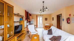 Ett kompakt bostadsutrymme med en tv, trämöbler, en matplats och ett kök.
