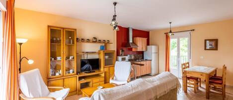 A compact living space with a kitchenette, a dining area, and a seating area with a TV and a lamp.
