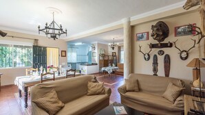 Uma sala de estar espaçosa com um sofá grande, um espaço de refeições e uma cozinha ao fundo.