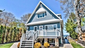 Une maison à deux étages avec un porche à l’avant, des fondations en pierre et un ciel d’un bleu limpide.