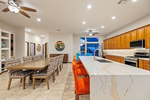 A modern kitchen with a large island, wooden cabinets, and a dining area with patterned chairs.