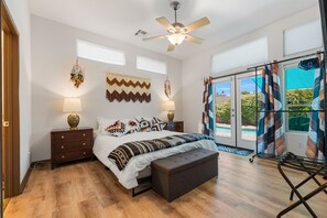 Une chambre à coucher avec un lit, des tables de chevet, un ventilateur de plafond et une vue sur l’extérieur.