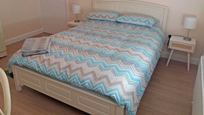Een keurig opgemaakt bed met een bedsprei met patroon, twee nachtkastjes met lampen, en een deur op de achtergrond.