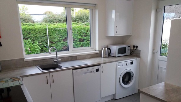 Een moderne keuken met witte kasten, een ingebouwde wasmachine, een magnetron en een raam met uitzicht op een tuin.