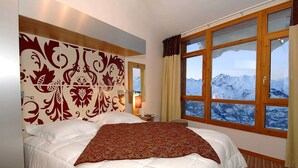 Habitación de hotel con una cama grande, un cabecero decorativo, una ventana con vistas a la montaña y una mesita de noche con lámpara.