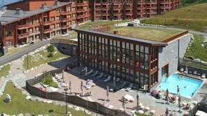 Un hotel de varios pisos, con piscina en la azotea y montañas al fondo.