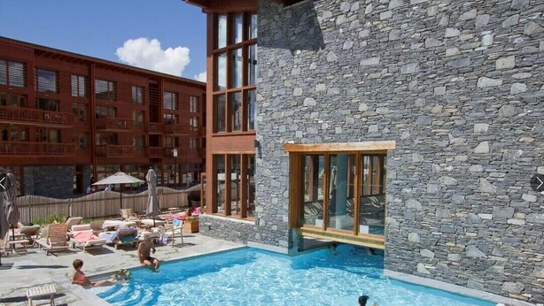 Zona de piscina con un edificio de piedra y una estructura de ladrillo rojo al fondo.
