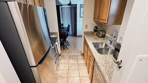 A kitchen with a stainless steel refrigerator, a sink, wooden cabinets, and a tiled floor.