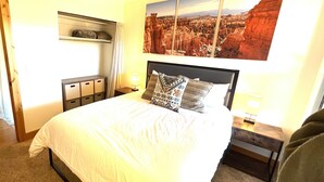 A hotel room with a large bed, a nightstand with a lamp, a wardrobe, and a painting of a canyon landscape on the wall.