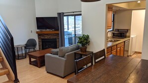 A modern kitchen with a built-in microwave, a dining area with a wooden table and chairs, a gray sofa, and a stone fireplace.