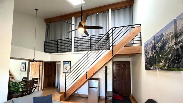 A spacious living area with a high ceiling, a wooden staircase, a dining area, and a refrigerator.
