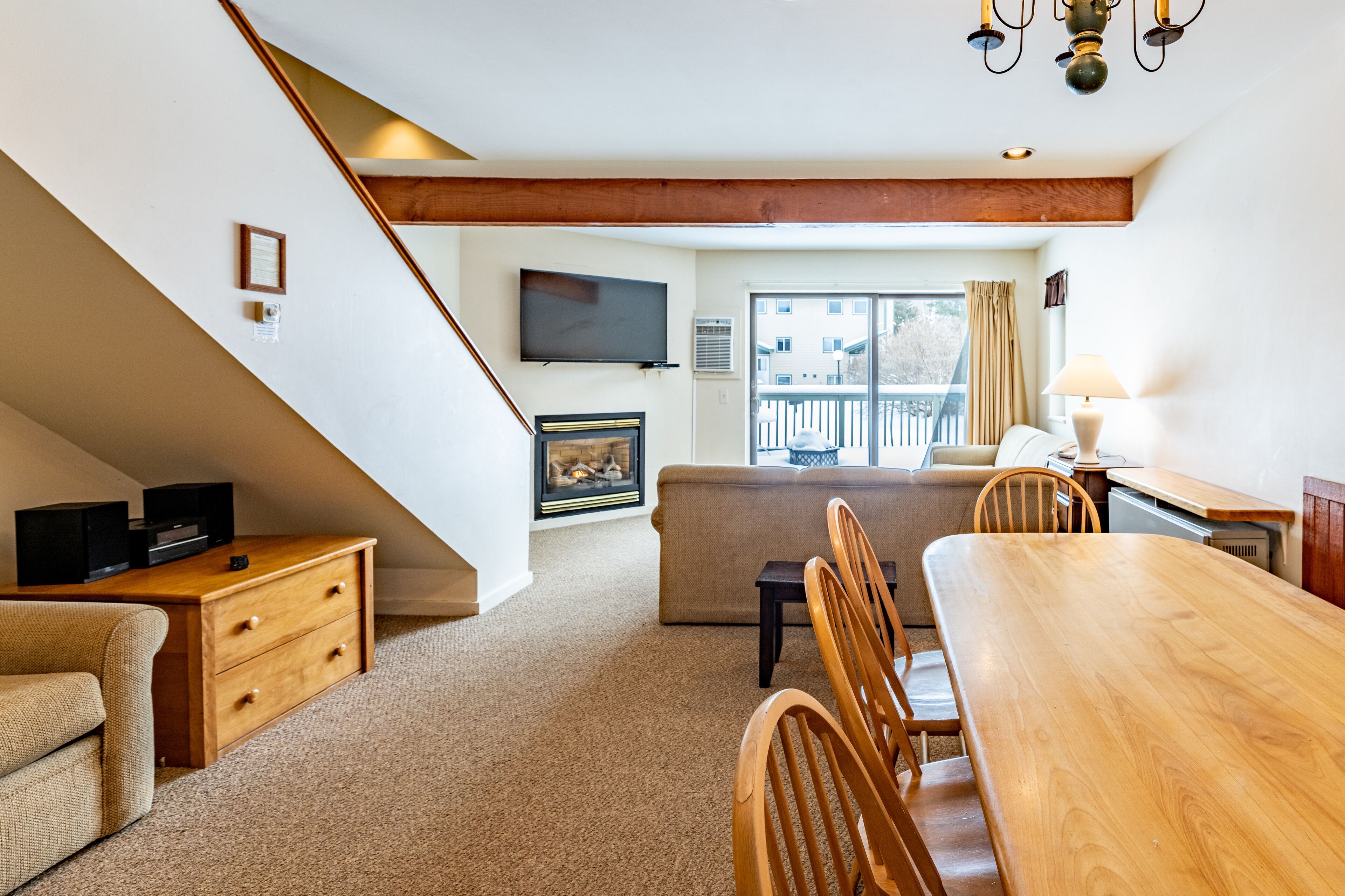 A spacious living area with a wooden dining table, a sofa, and a television mounted on the wall.