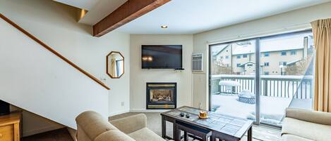 A living room with a fireplace, a television, and a balcony with a view of buildings.
