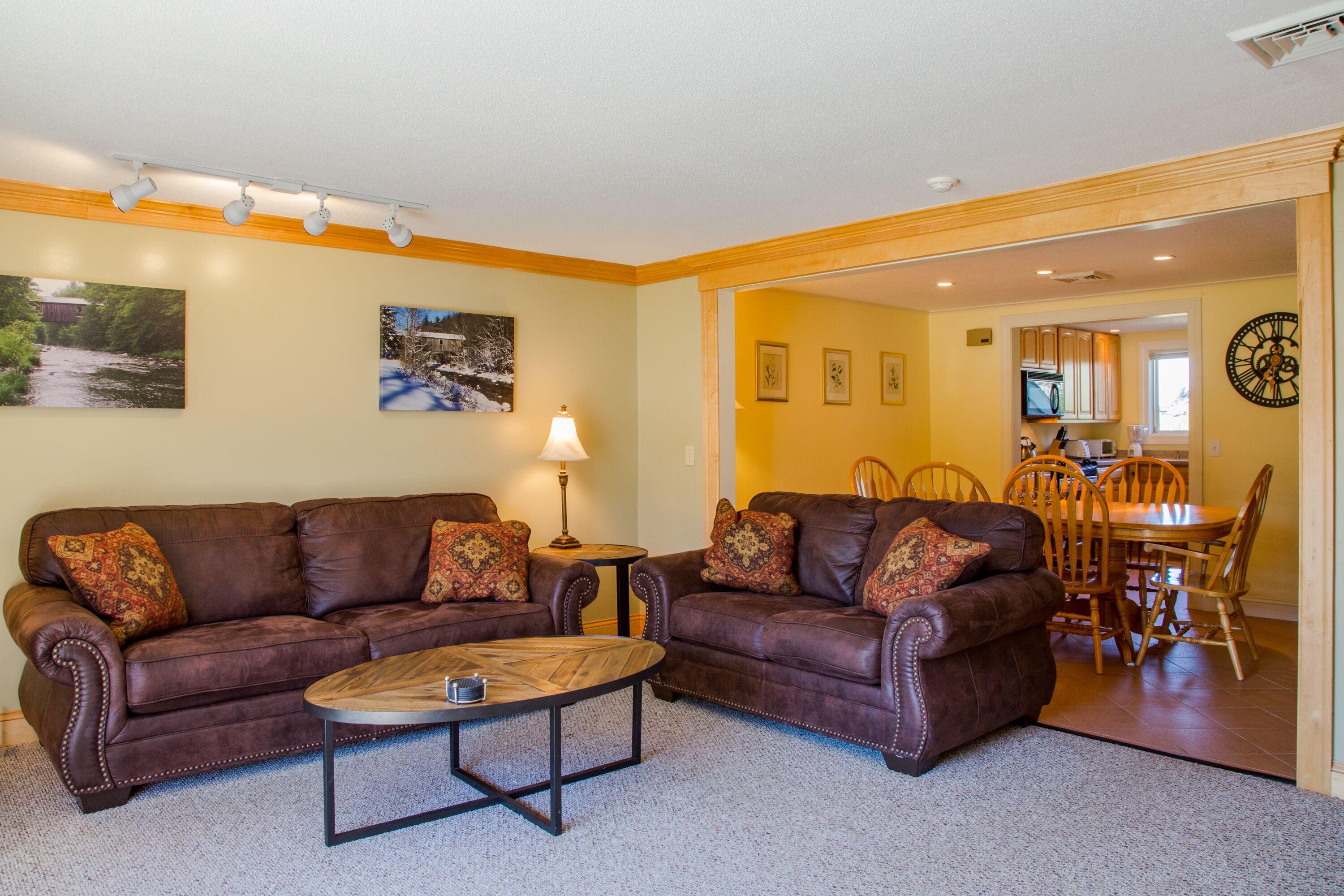A living room with two brown leather sofas, a coffee table, and a dining area with wooden chairs and a table.