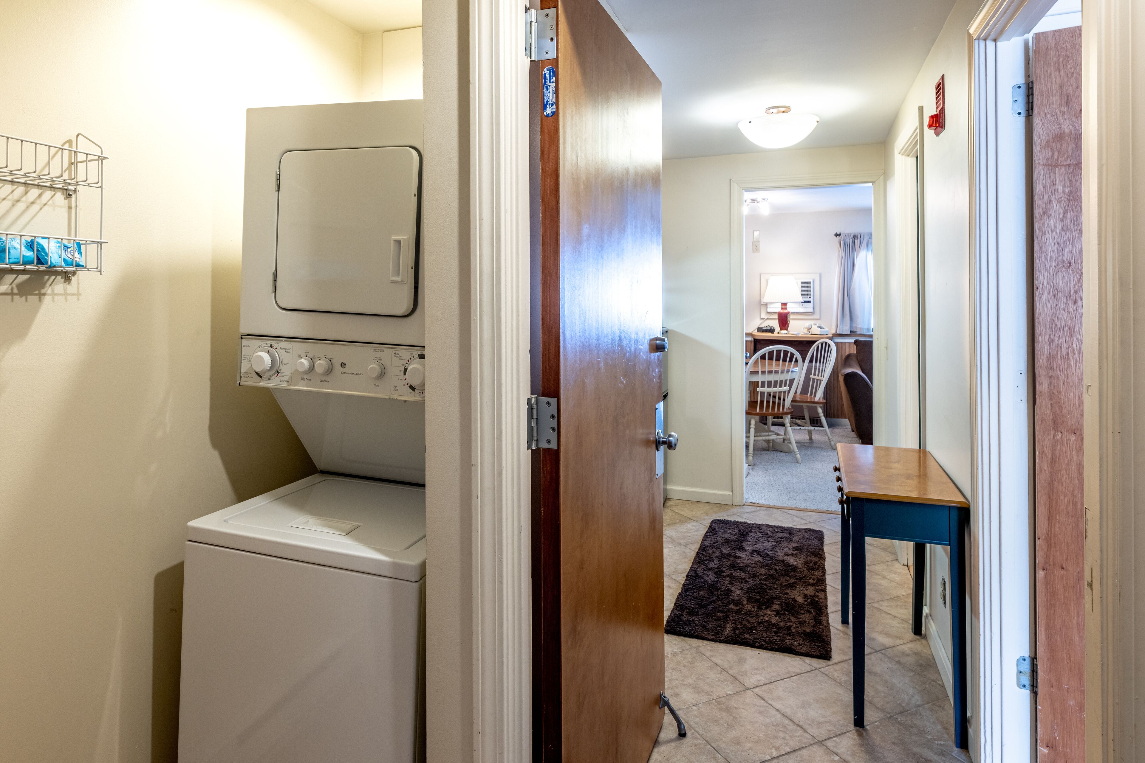 A laundry room with a washer and dryer, a wooden door, a dining area with a table and chairs, and a kitchen in the background.
