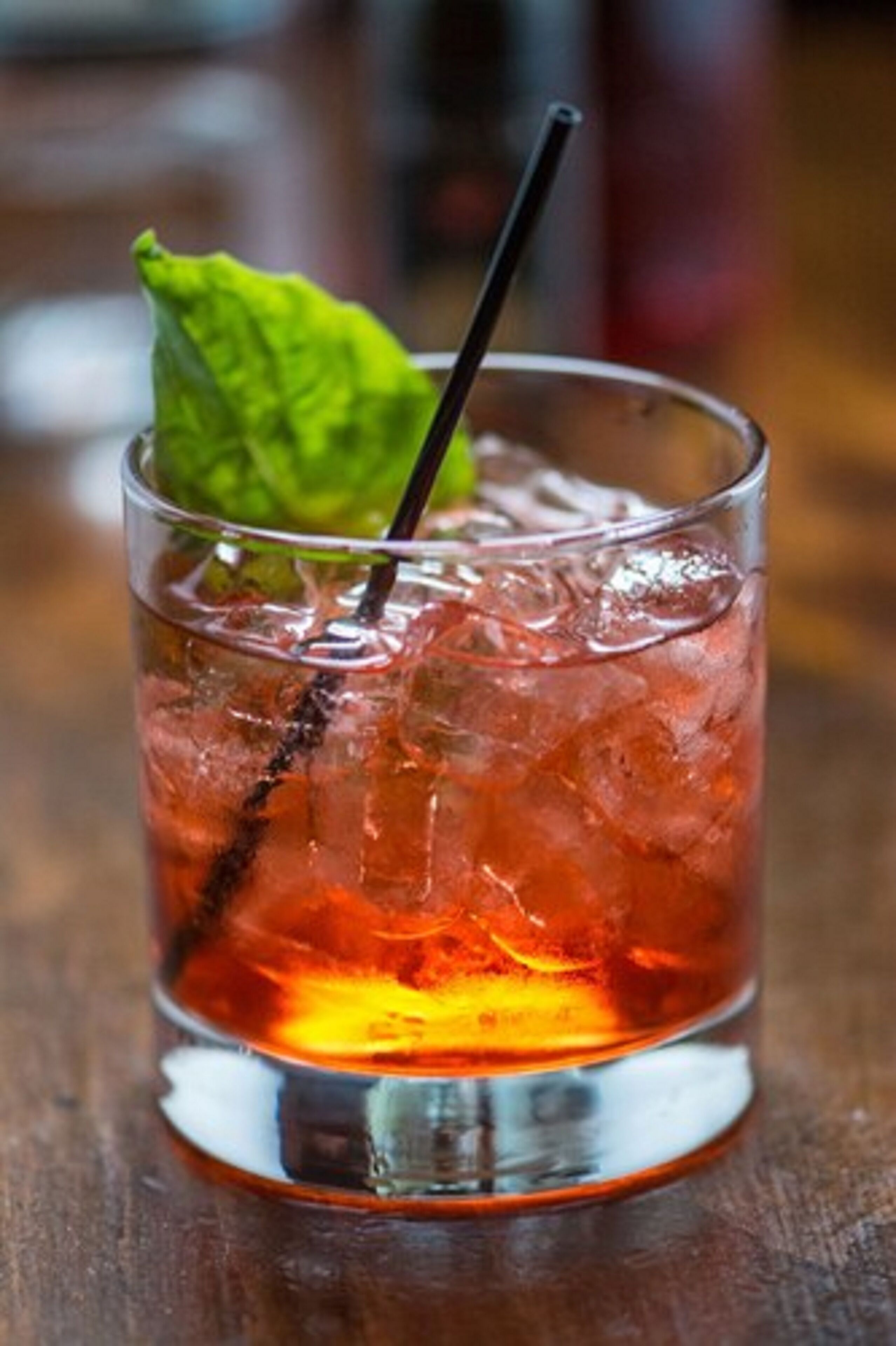 A glass of iced beverage with a mint leaf garnish and a straw, placed on a wooden surface.