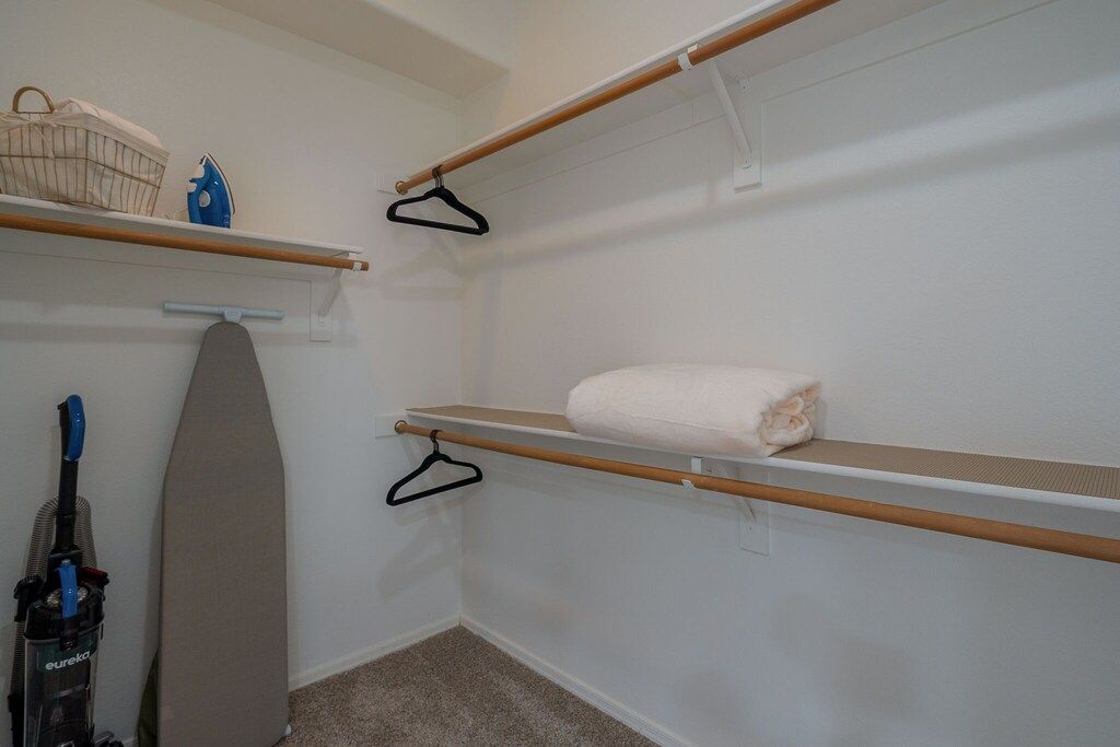 A small, neatly organized laundry room with shelves, an ironing board, and a vacuum cleaner.