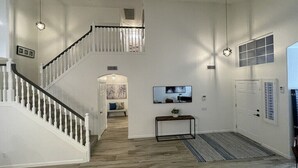 Een ruime woonkamer met een trap, een flatscreen-tv aan de muur en een console tafel met een plant.