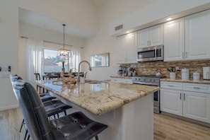 A modern kitchen with white cabinets, a large island with bar stools, a stainless steel microwave, and a tiled backsplash. - Stunning $100K+Remodel! Perfect QuietLocation,HtdPool,Spa,BBQ,FirePit,EV Charger (Scottsdale)