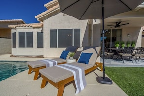 A poolside area with two lounge chairs and a table, a patio umbrella, and a view of a house with large windows. - Stunning $100K+Remodel! Perfect QuietLocation,HtdPool,Spa,BBQ,FirePit,EV Charger (Scottsdale)