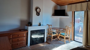A cozy room with a fireplace, wooden furniture, a television, and a view of the outdoors.
