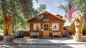 A wooden cabin with a sign reading "OFFICE" and an American flag. There are two benches outside and a wooden statue of a bear on a stump.