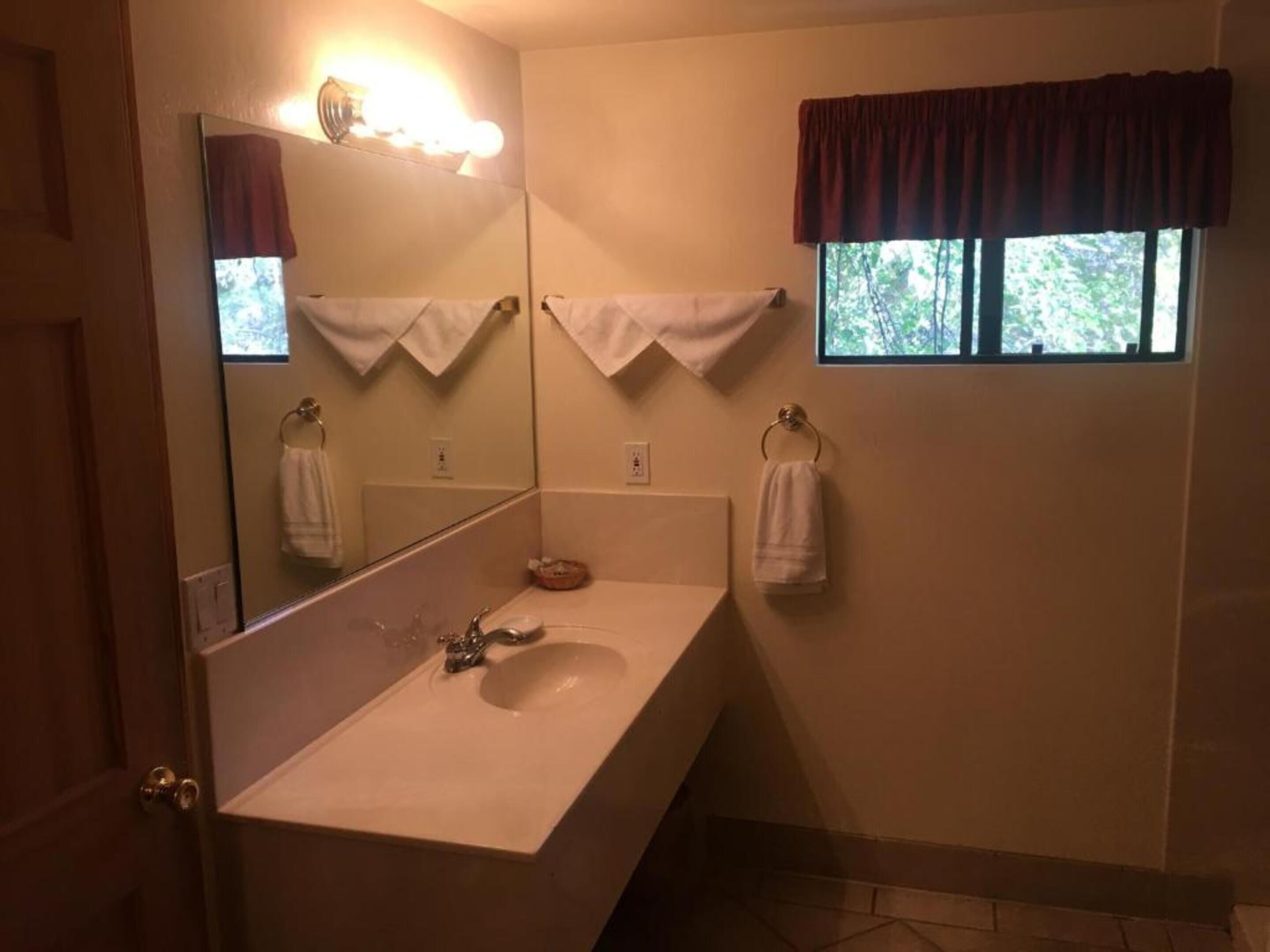 A bathroom with a large mirror, a sink, and two towels hanging on hooks.
