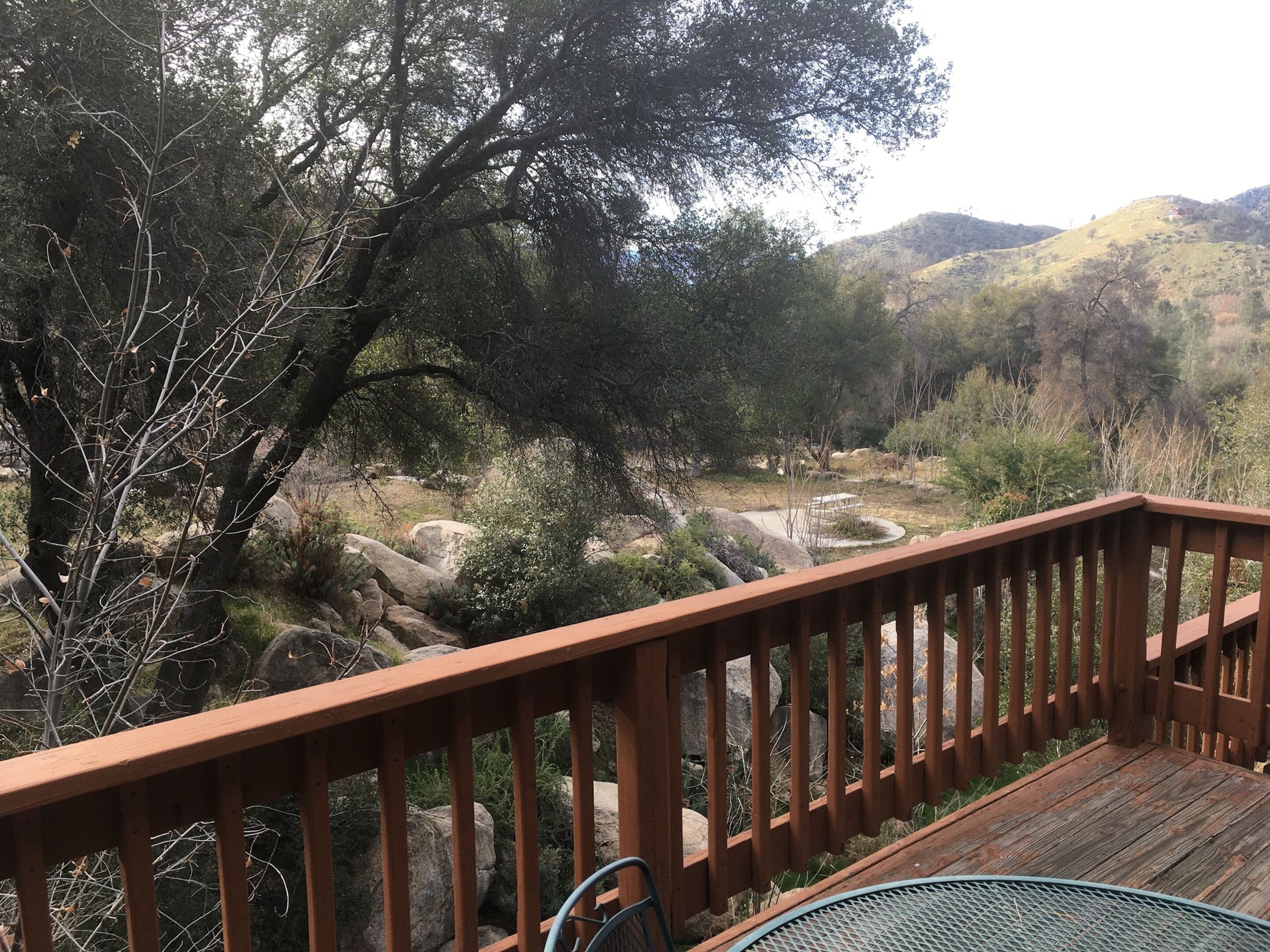 A wooden deck with a metal chair, overlooking a rocky landscape with trees and hills.