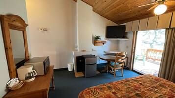 Une chambre avec un lit, un bureau, une chaise, une télévision et un ventilateur de plafond.