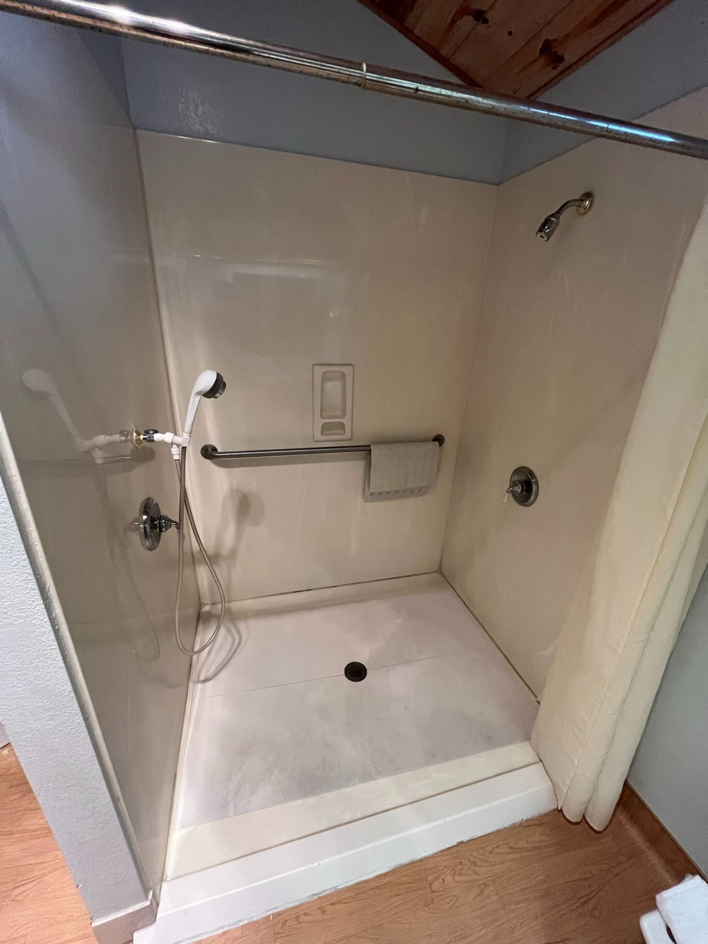 Un espacio de ducha pequeño y cerrado con puerta de vidrio, un perchero para toallas y un cabezal de ducha.