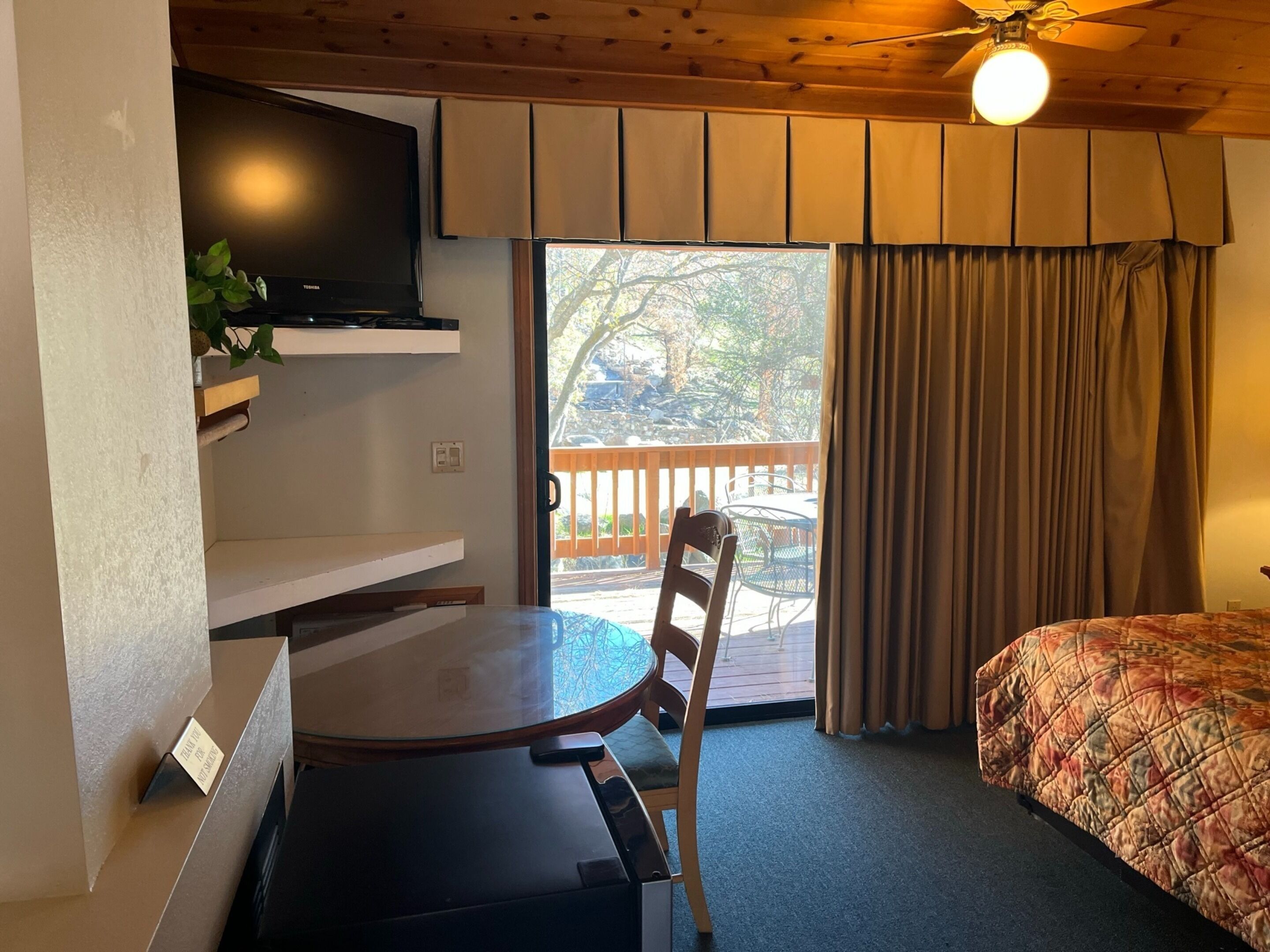 Une chambre d’hôtel comprenant un lit, un téléviseur fixé au mur, une table à manger avec des chaises et une vue sur l’extérieur grâce à une porte coulissante.