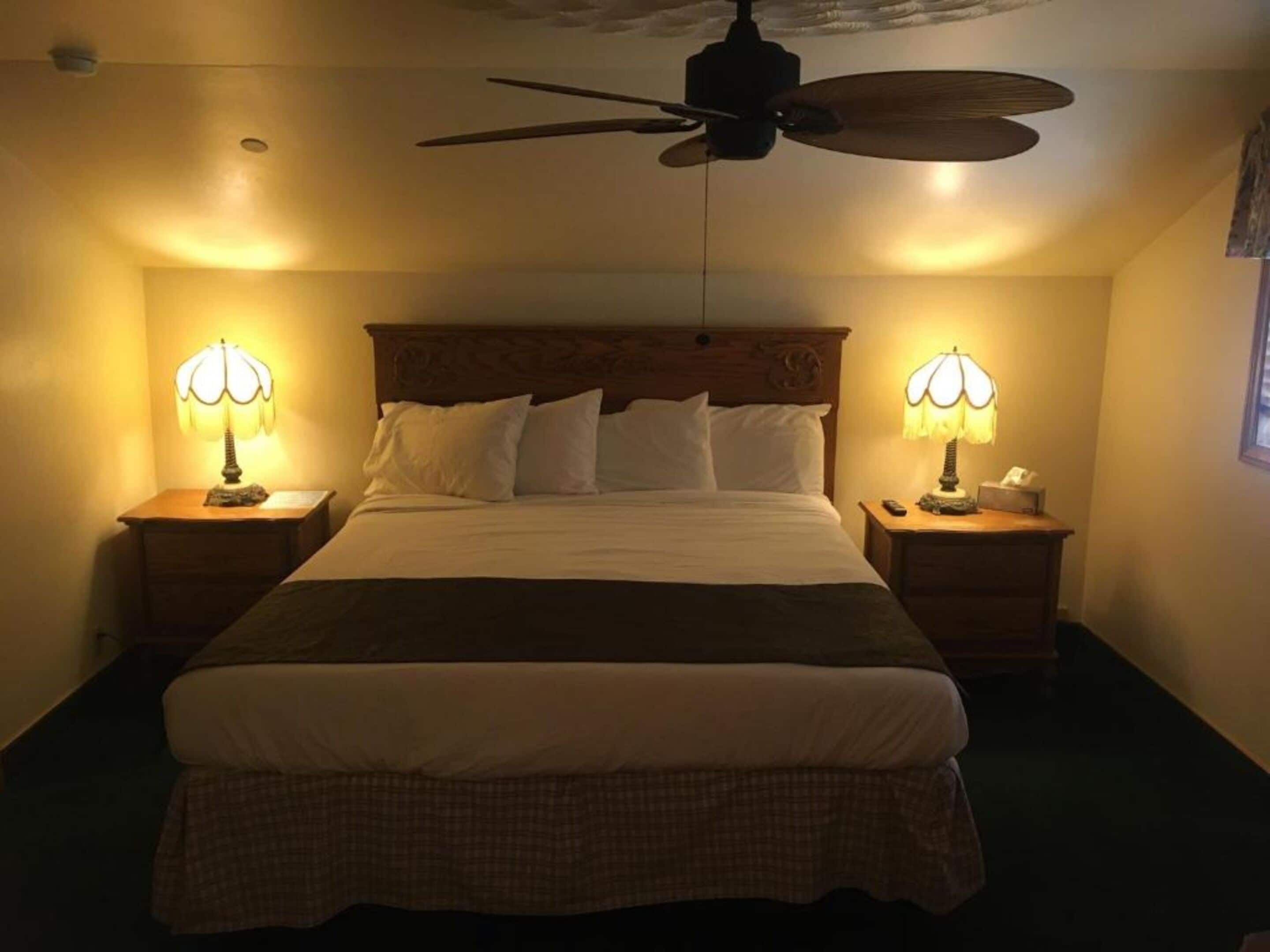 A hotel room with a large bed, two bedside tables with lamps, a ceiling fan, and a window.