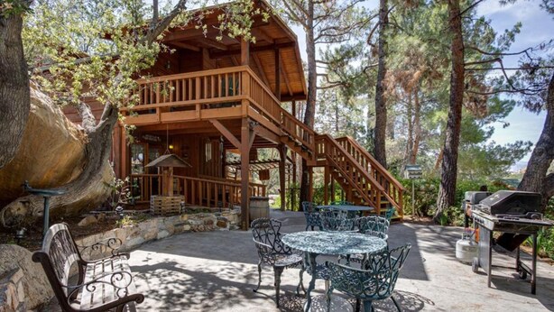 A wooden cabin with a balcony, outdoor seating, and a grill area.