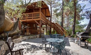 A wooden cabin with a balcony, outdoor seating, and a grill area. - Whispering Pines Lodge (Kernville)