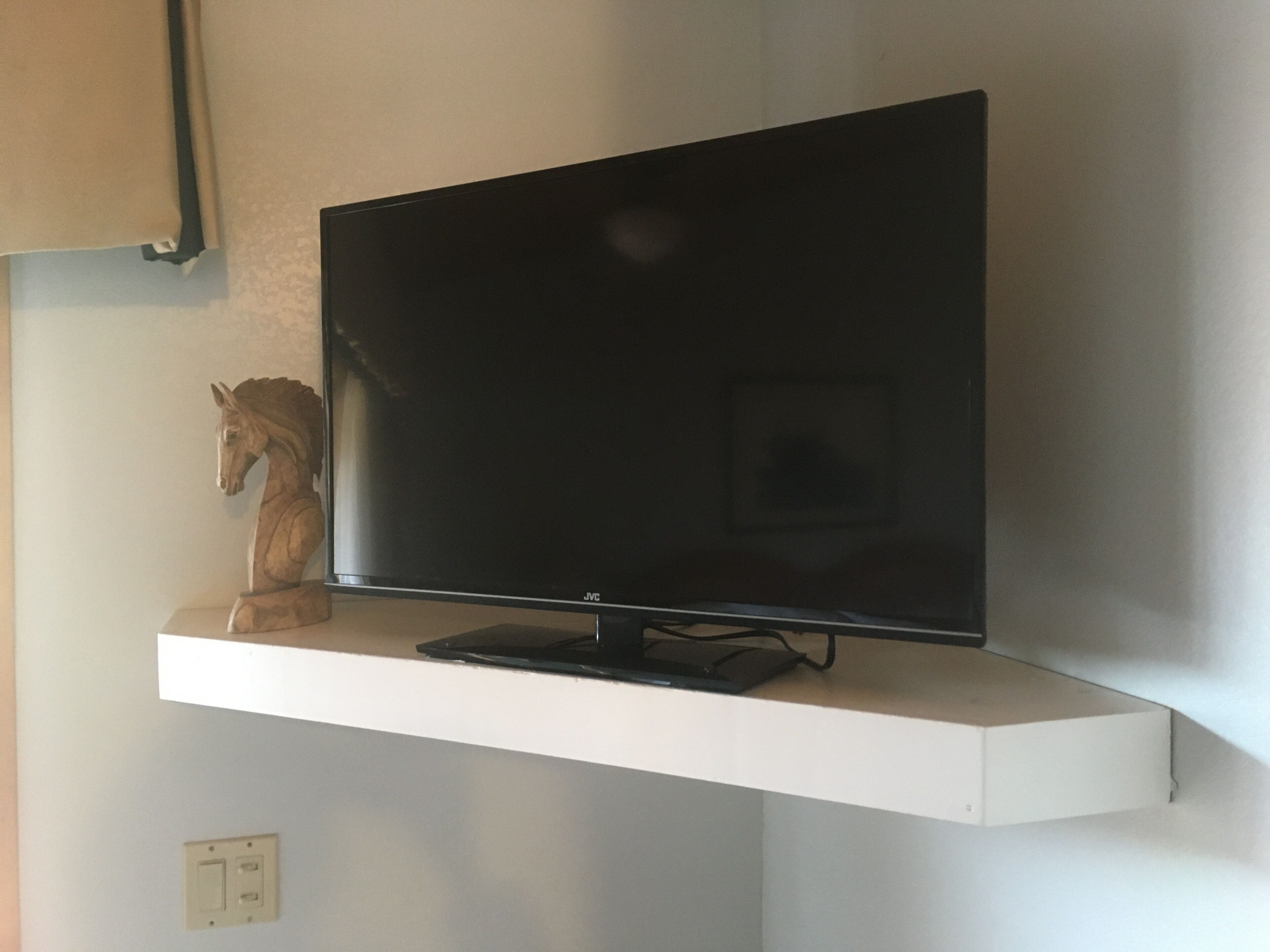 A flat-screen TV on a white shelf with a wooden horse sculpture beside it.