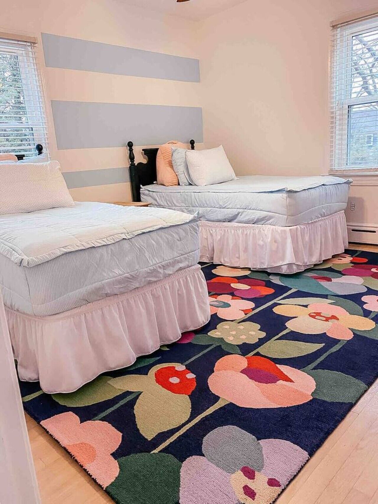 A bedroom with two beds, a colorful floral rug, and a striped wall.