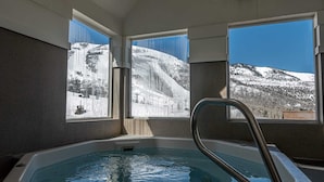 Ein Whirlpool mit Blick auf eine verschneite Berglandschaft durch große Fenster.