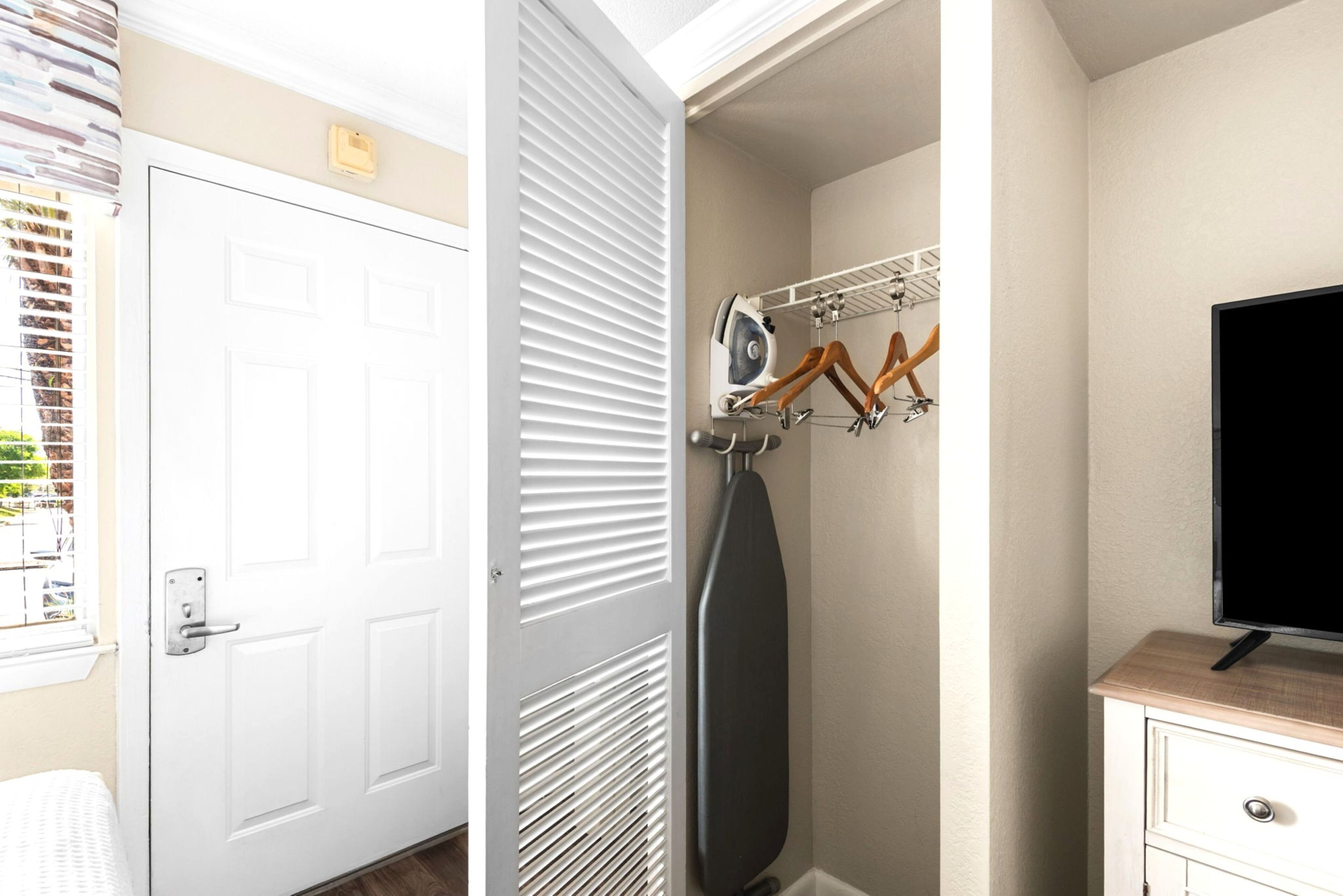 A room with a white door, a clothes drying rack, a television, and a small wooden cabinet.