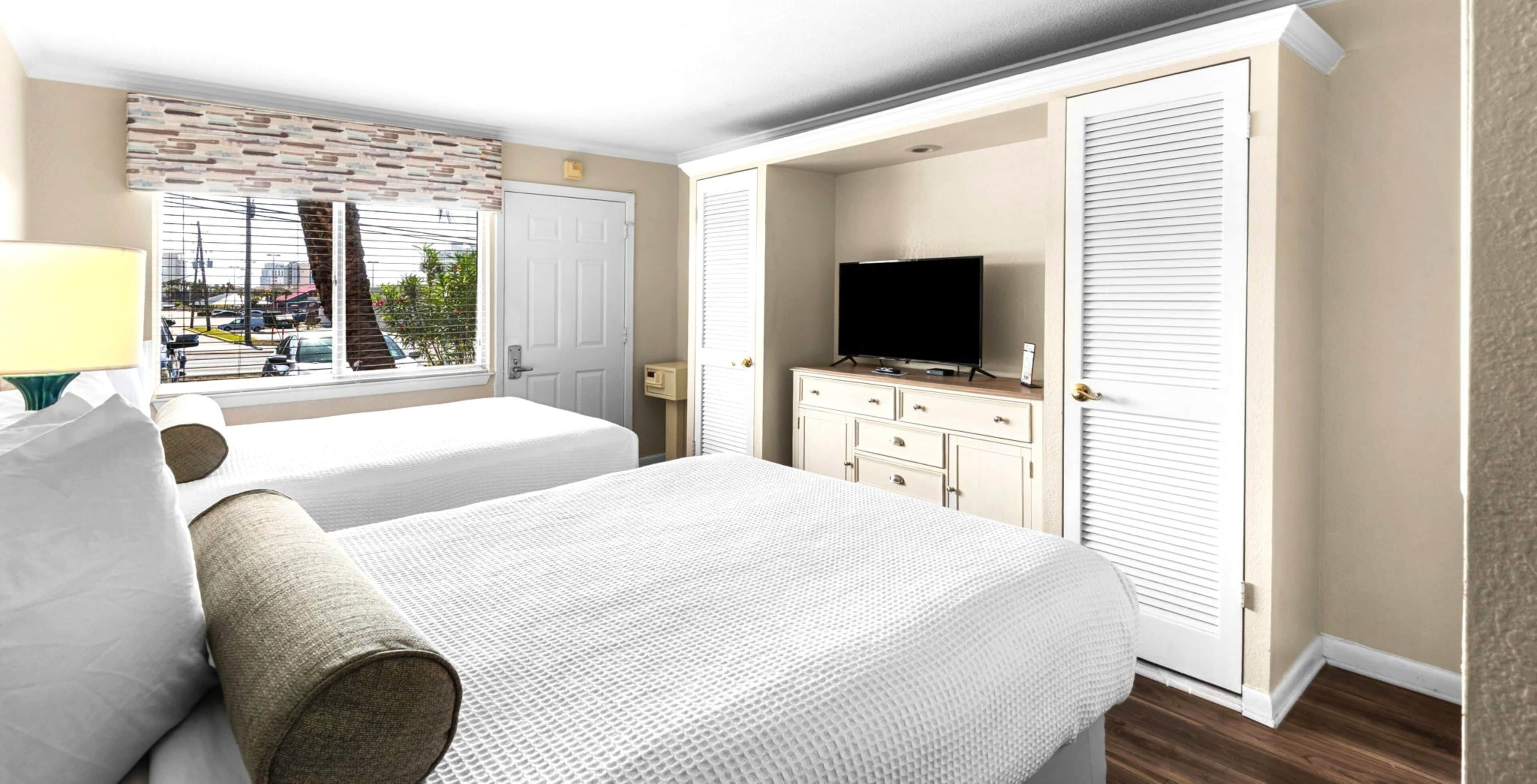 A hotel room with two beds, a TV, a dresser, and a window with a view of the outside.