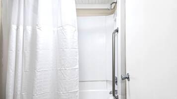 A shower area with a white shower curtain, a glass door, and a metal grab bar.