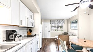 A kitchen with white cabinets, a coffee maker, and a dining area with a table and chairs. - Club Destin Condos (Destin)