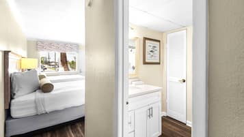 A hotel room with a bed, a window with a view of the street, a bathroom with a sink and mirror, and a door.