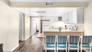 A modern kitchen with white cabinets, a granite countertop, and a built-in microwave. - Club Destin Condos (Destin)