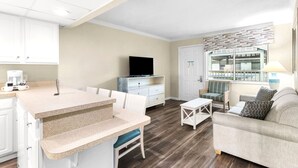 A modern living room with a sofa, a coffee table, a TV, and a kitchen area with a counter and cabinets. - Club Destin Condos (Destin)